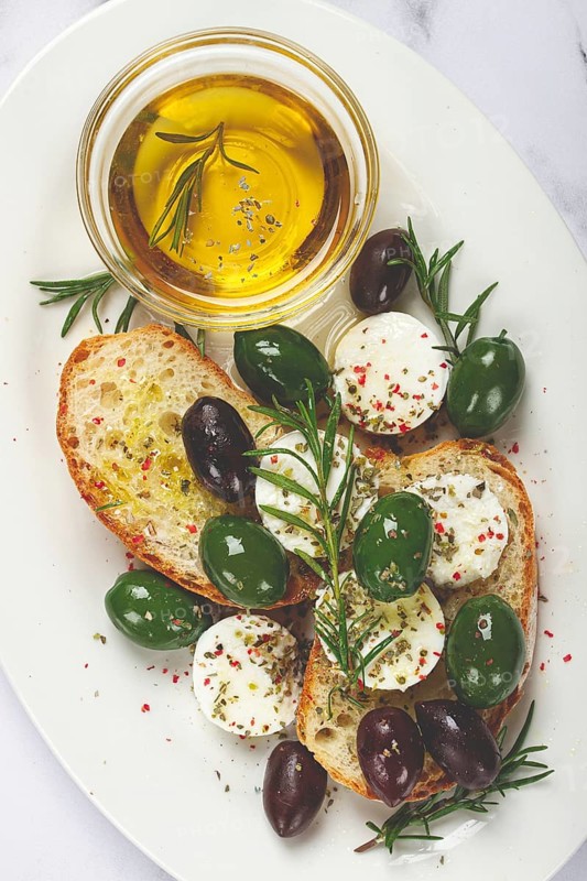 A plate with a snack, ciabatta bread with cheese and olives, olive oil, spices and herbs, top view, no people