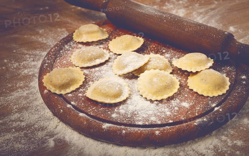 Fresh raw, uncooked ravioli, on a cutting board, with a rolling pin for dough, wooden background, no people
