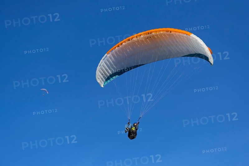 Paraglider with orange wing flies freely under a clear blue sky