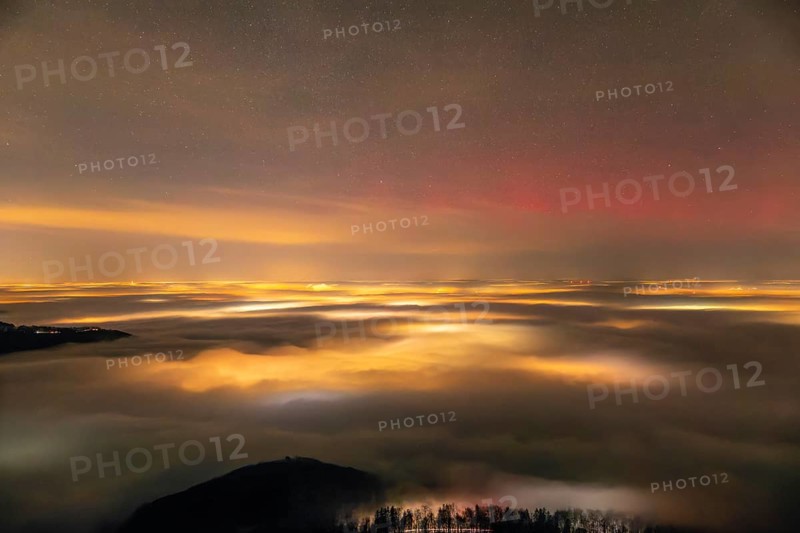 Firework lights under the sea of fog. New Year's Eve fireworks 2024 and a little red Aurora Borealis Northern Lights. On the Breitenstein, Swabian Alb near Ochsenwang. Sea of fog in the foothills of the Alb. View towards Stuttgart. In the foreground Hahnenkamm and on the left the Hörnle looks out of the fog