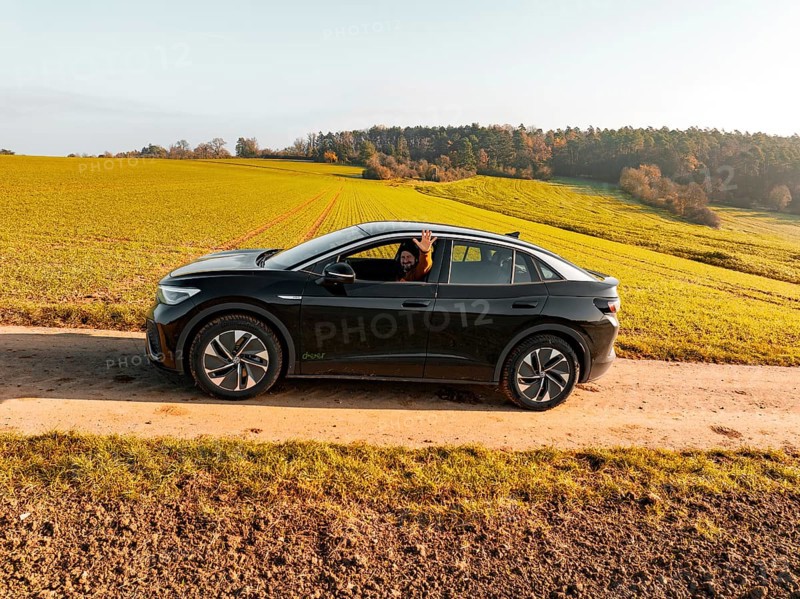 A driver sits in a black car on a dirt track, surrounded by green meadows, electric car VW ID5, Deer Carsharing, Gechingen, Black Forest, Germany, Europe