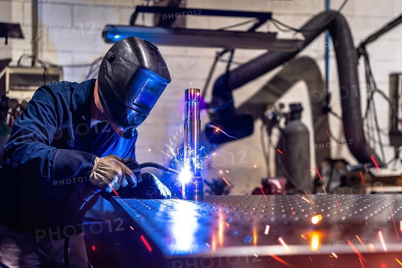 Unrecognizable man with safety goggles and gloves working in a factory welding pieces of metal