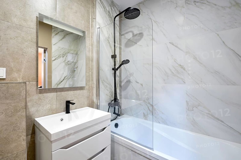 A beautifully designed bathroom showcases marble walls and a stylish shower-bathtub combo. A modern vanity with a mirror adds functionality and elegance to the space