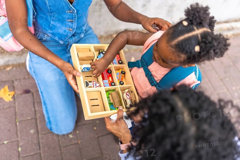 Top view close-up of an african girl picking toys from a box in the street next to her mother and grandmother in a residential area