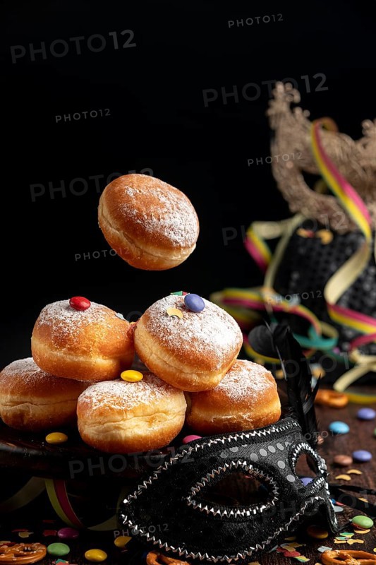 Berliners, doughnuts with icing sugar and Smarties next to a black mask, carnival