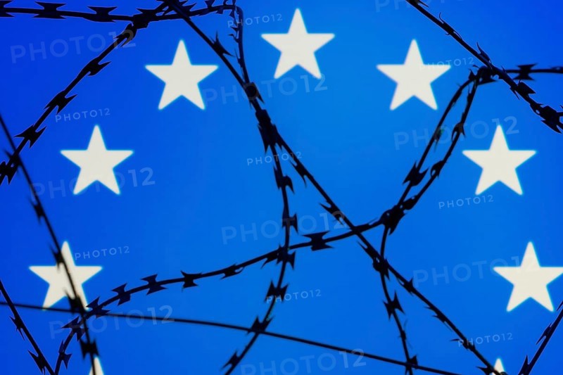 Symbolic image, migration, defence against refugees wanting to enter the EU, barbed wire overarches the stars of the EU flag against a blue sky, border, border fence