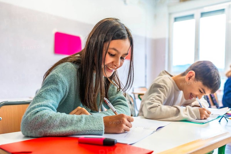 Happy elementary age children writing enthusiastically in notebooks during class, engaging with lessons and enjoying their school experience