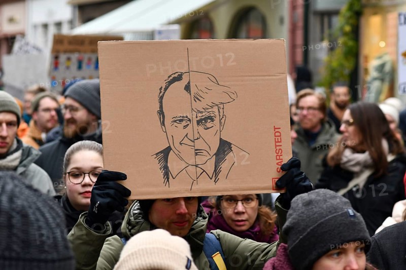 Heidelberg, Germany - February 12th 2025: Person holding up sign comparing CDU politian Friedrich Merz to USA president Donald Trump in crowd at protest against far-right