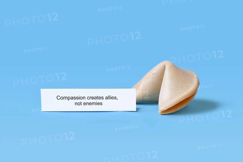 Fortune cookie with motivational text saying 'Compassion creates allies, not enemies on blue background