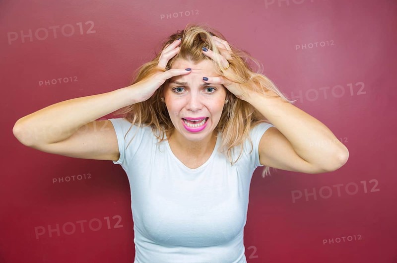 Concept of worry, woman with both hands on head on red background