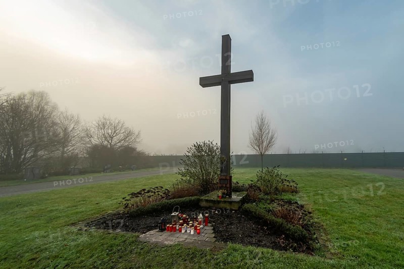 Simple wooden cross in foggy cemetery with red and white votive candles at its base