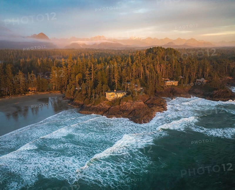 Aerial view of ocean waves crashing against a forested coastal island at sunset, with warm light illuminating the scene, Panorama shot, Tofino, BC, Canada, North America