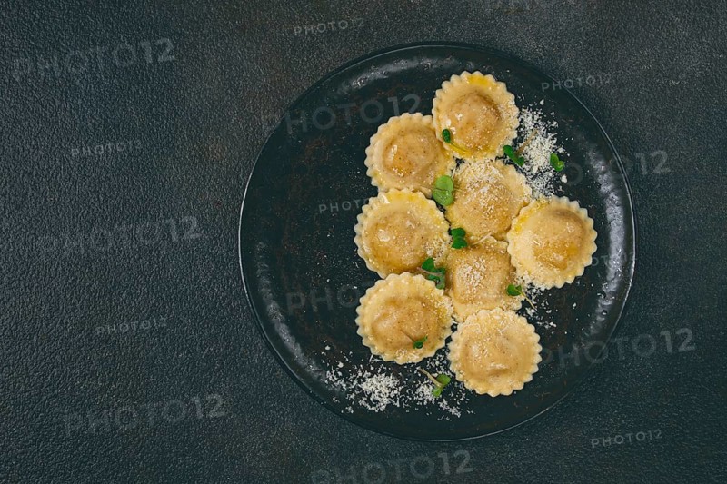 Fresh ravioli with cheese and microgreens, on a black plate, top view, no people
