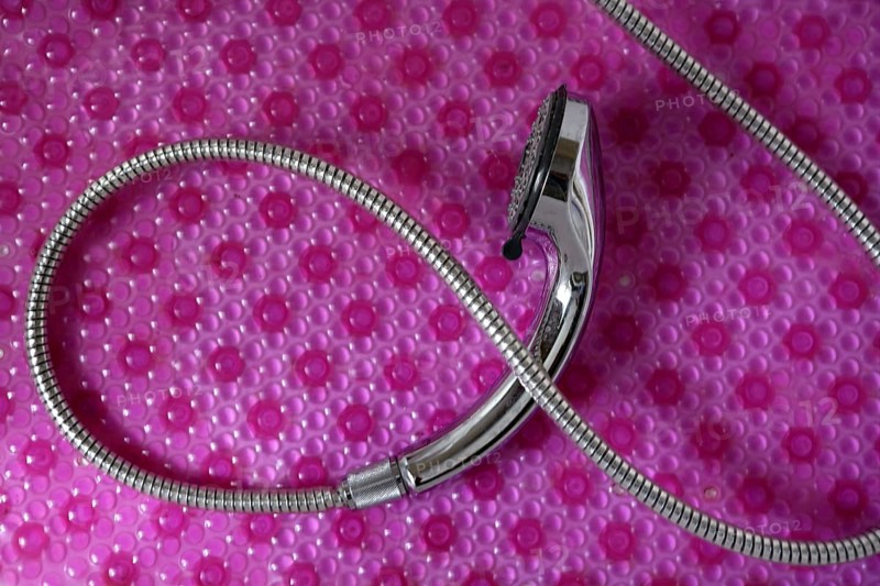 Bathroom chrome shower head with silver hose over pink background