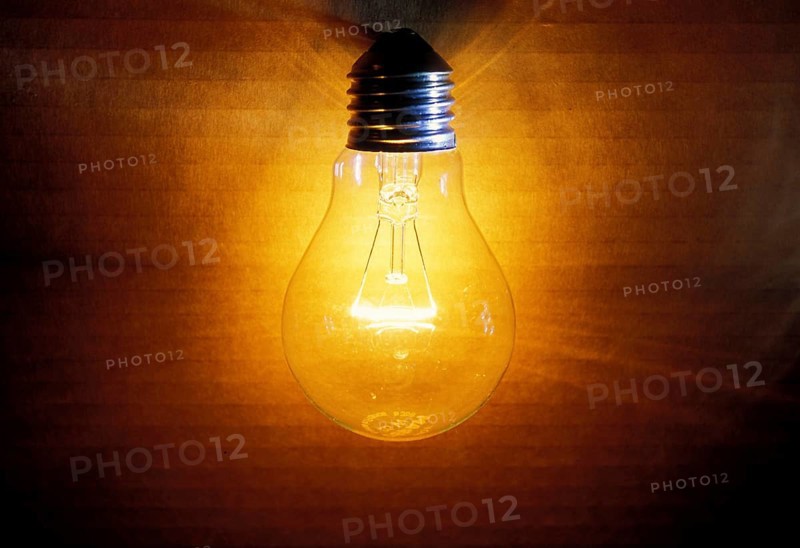 Closeup of an old burning light bulb, switched on, a carton as background is illuminated, lit with a warm yellow and orange light