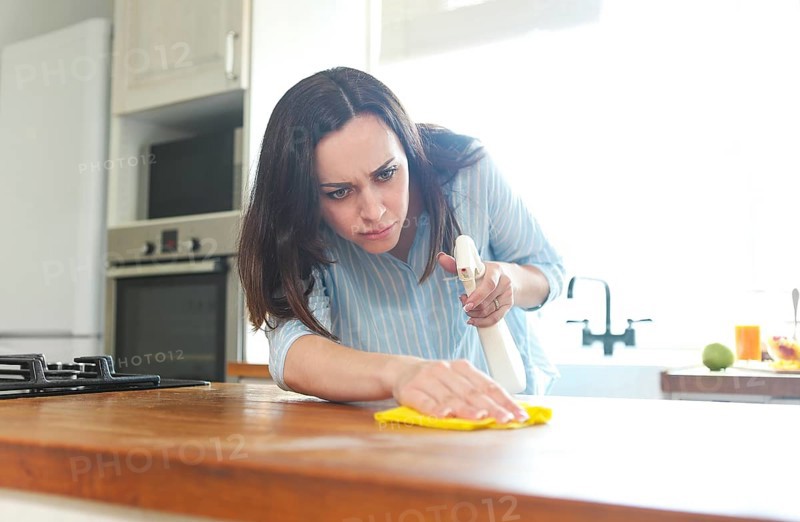 Brunette woman with rag and spray bottle cleaning wooden counter-top
