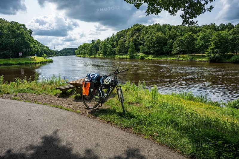 A bicycle stands on a cycle path next to a peaceful river in nature, cycle tour along the Ems and Emsaltarm-Roheide