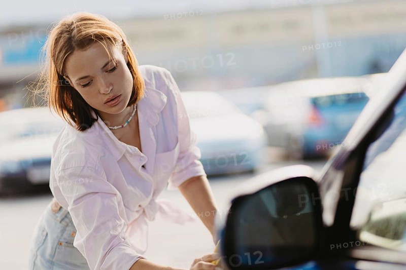Woman concentrating while cleaning a car window with a sponge under sunlight