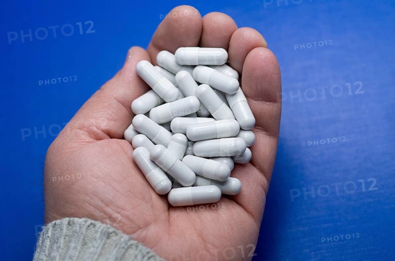 Large white pills fell from a large white bottle. Concept of drugs. Life without drugs and dependence on capsules of antibiotic, medicine, amphetamines, drugs and drugs. A male hand throws antibiotic capsules against a blue background. Bulgaria