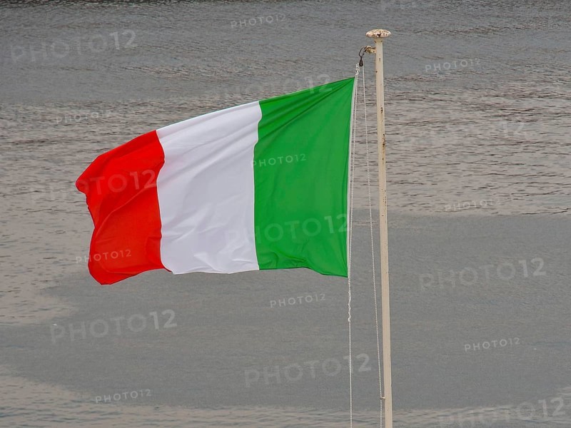 Italian flag waving in the wind in front of a body of water, naples, mediterranean sea, italy