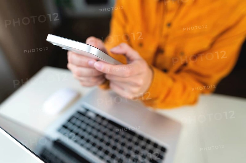 Female student's hands with a phone on the background of a modern laptop and desktop. Freenacer working from home, hipster profession