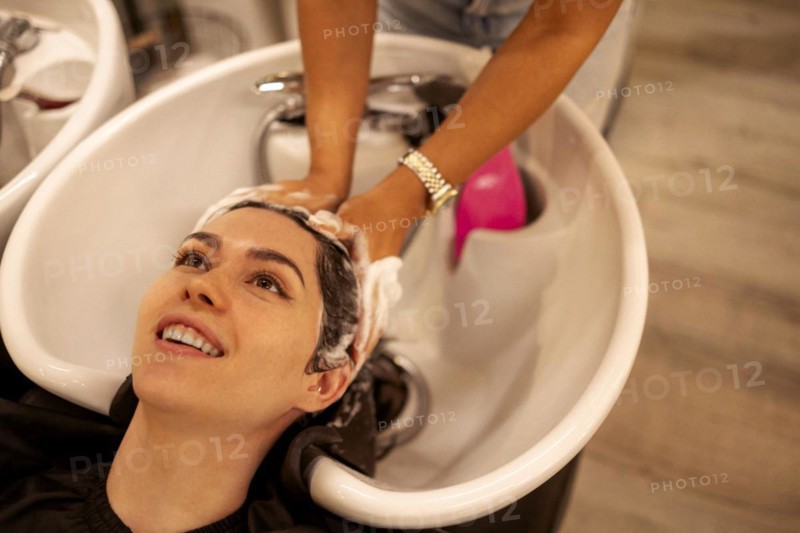 Cheerful young brunette womn enjoying head massage and washing hair while getting her haircare