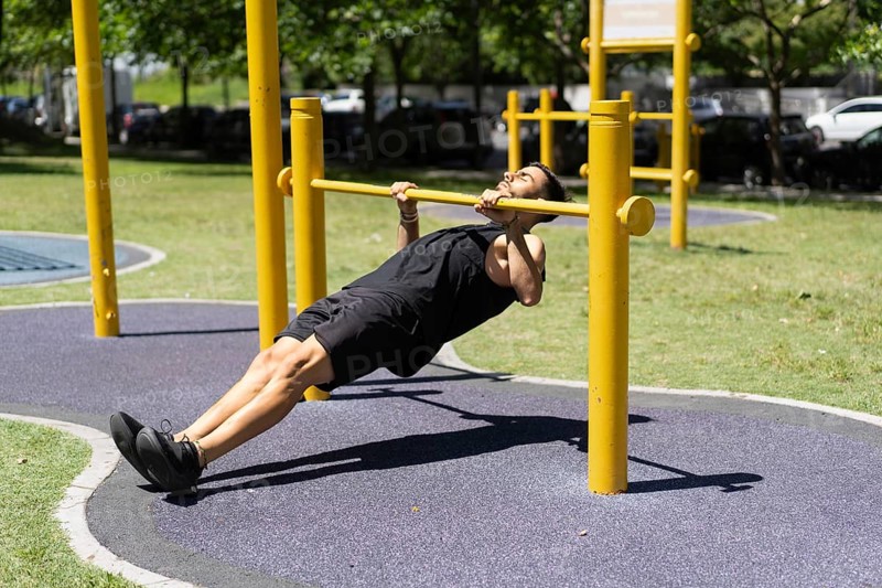 Young man performing inverted rows on outdoor bars.