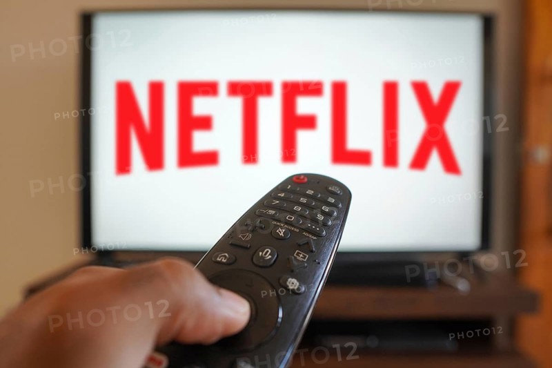 April 20, 2024, Brazil. In this photo illustration, a hand holding a TV remote control in front of the Netflix logo on a TV screen