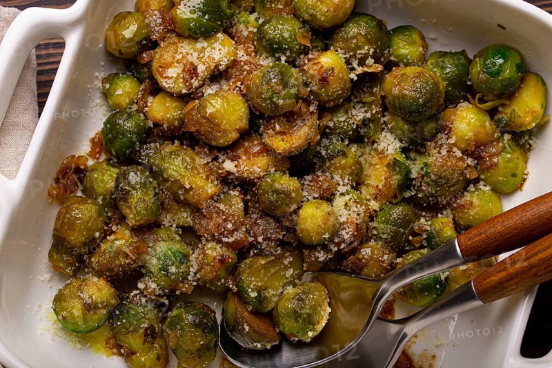 Healthy vegetarian dish roasted brussels sprouts with butter and parmesan cheese in white ceramic casserole top view on dark rustic wooden table from above, vegan food