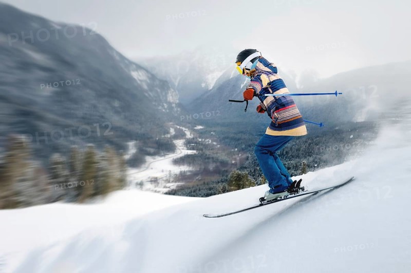 A female athlete skier rides a freeride in a winter forest in the mountains. Jump against the backdrop of snow-covered trees and the setting sun