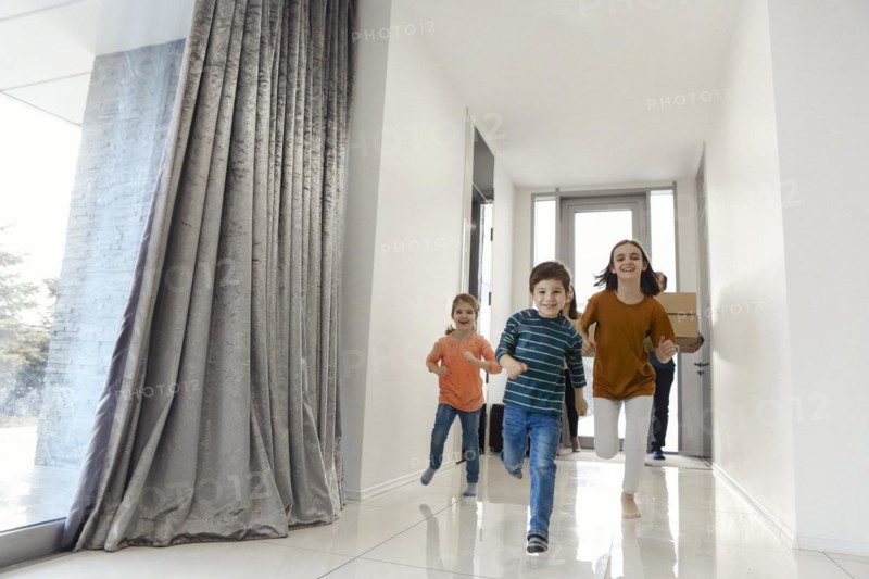 Happy family running in hall. Funny kids jumping with carton box, parents laughing, play with children have fun together move at new house. Mortgage loan and relocating concept