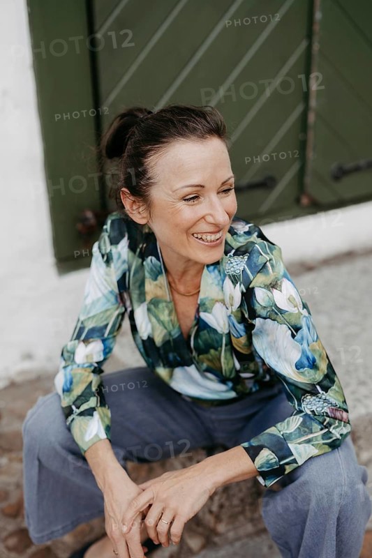 Smiling, dark-haired woman, 40+, sitting on a staircase