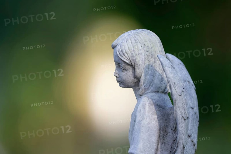 Sad looking little angel figure on a gravestone in front of atmospheric bokeh in the background