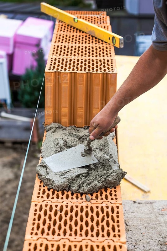 Anonymous construction worker on a building site erecting a brick wall. Brick wall of a solid house. Symbolic image for illegal labour and bungling