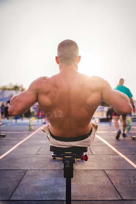 A man exercises outdoors in the sunlight, concentrating on strengthening his back muscles on a rowing machine, Barcelona, Spain, Europe