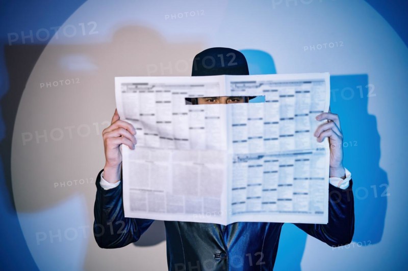 Man hiding watches through the newspaper in the spotlight on studio background. noir film style. Private detective, investigation, secret, detective, espionage concept