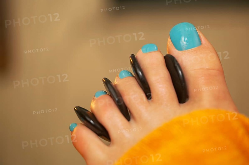 Close-up shot of female feet with blue toe nails getting spa hot stone therapy at beauty treatment salon