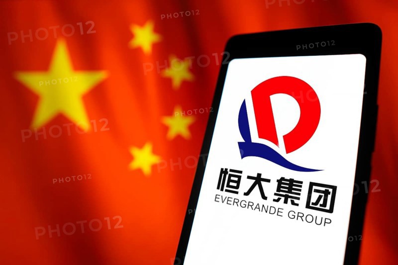 In this photo illustration, the Evergrande Real Estate Group logo is displayed on a smartphone screen and in the background, the flag of China