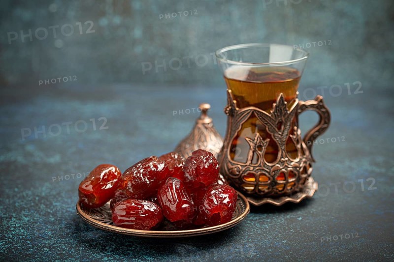 Breaking fasting with dried dates during Ramadan Kareem, Iftar meal with dates and Arab tea in traditional glass, angle view on rustic blue background. Muslim feast, food photography, food photography