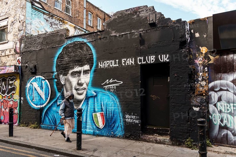 London, UK, August 25, 2023: Street scene with people walking by Brick Lane in Shoreditch Area in the East End. Maradona graffiti painted on walk on background