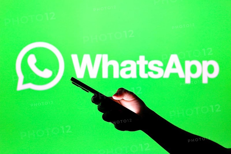 In this photo illustration the WhatsApp logo seen in the background of a silhouette hand holding a smartphone