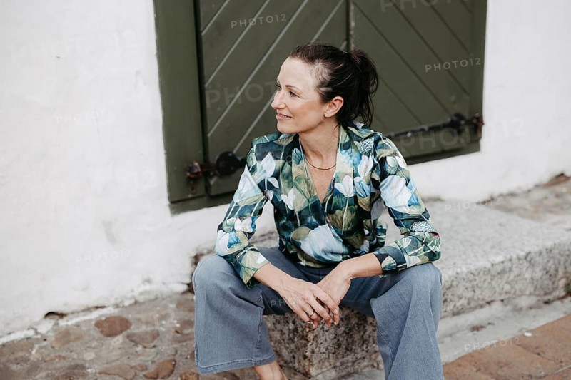 Smiling, dark-haired woman, 40+, sitting on a staircase