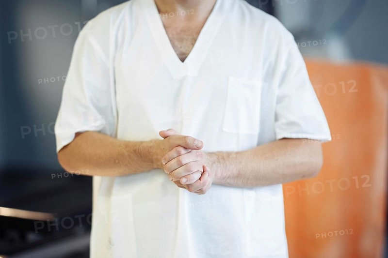 A man in a white hospital gown with hands clasped, conveying calmness in a medical setting
