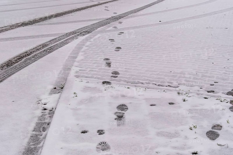 Fresh snow covers a cobblestone street with footprints and tire tracks crossing, creating a winter urban scene