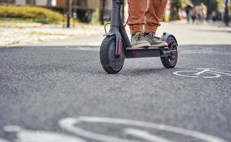 Young man in casual trousers riding an electric scooter detail on his feet and wheel over asphalt road, Liptovsky Mikulas, Slovakia, Europe