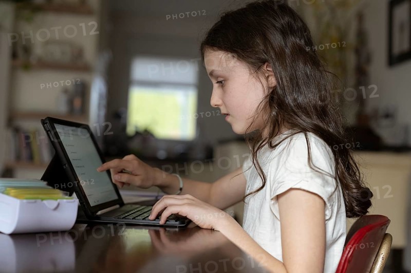 Girl, 10 years old, sits at the table with a tablet and learns