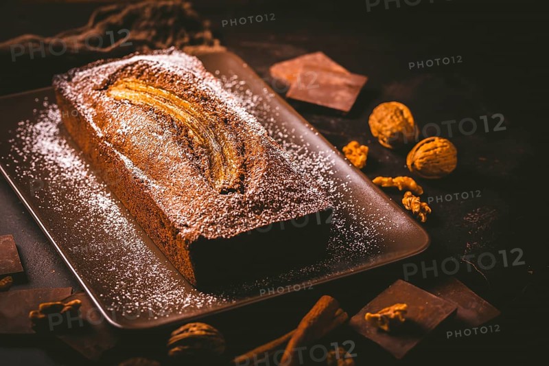 Homemade vegan banana bread or cake with nuts, chocolate and cinnamon on brown background