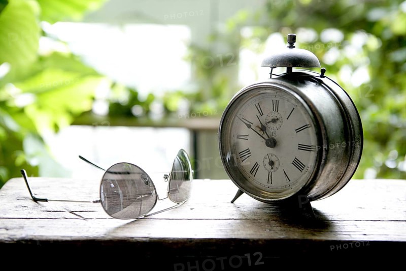 Old alarm bell clock at the window backlit in a house room with plants