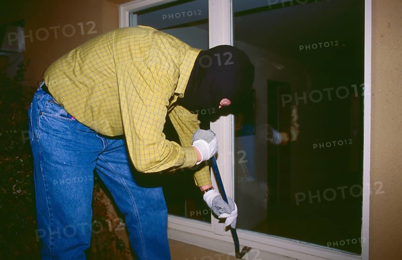 A masked burglar breaks into a house at night with a crowbar