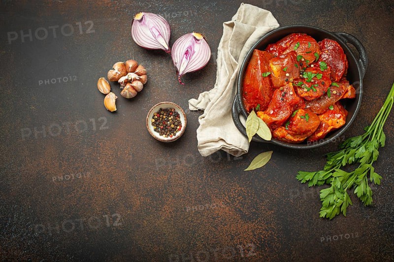 Cooking hearty meat stew. Raw uncooked chopped pieces of meat marinated with seasonings and parsley in black casserole dish top view, ingredients on dark rustic background. Space for text, food photography, food photography